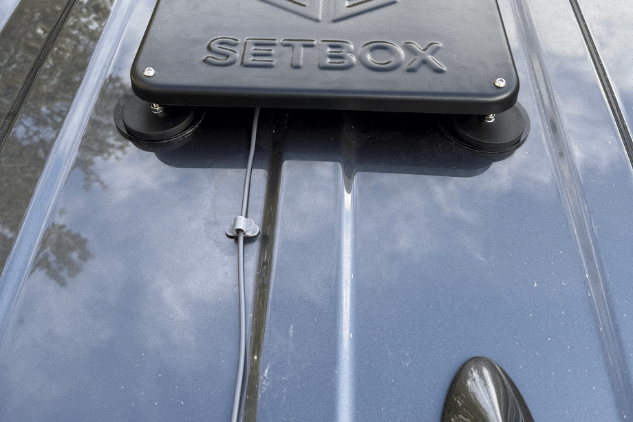 Black housing on a roof rack, cable routed along the rail