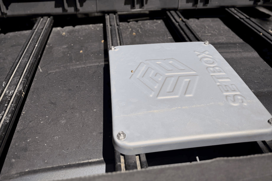 Grey SETBOX housing on a vehicle roof rack in a pine forest
